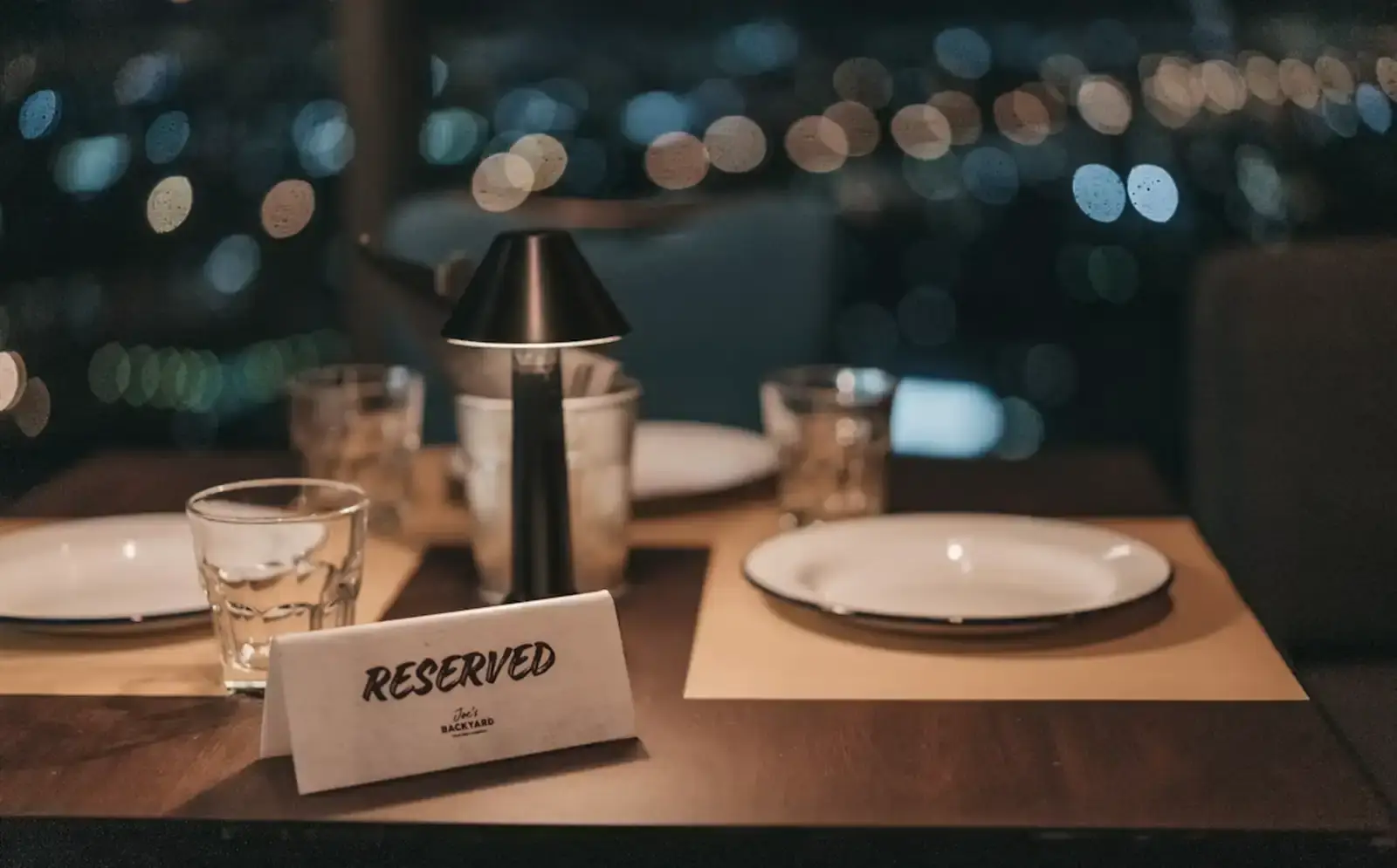 Mesa posta à noite com pratos, copos e luminária